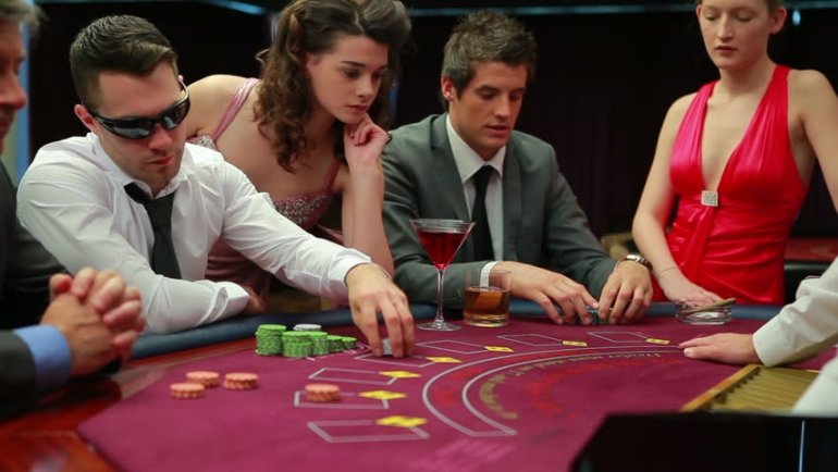 Серьезные мужчины ведут игру в блщэкджек, а девушки в откровенных нарядах наблюдают за игорным столом