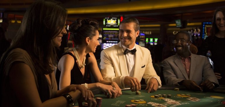 Женщины в вечерних платьях и мужчина в строгом костюме проводят время в казино
