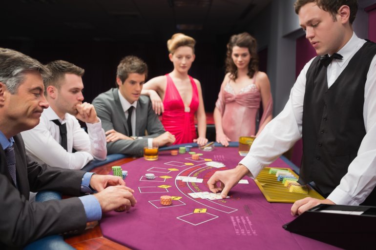 Молодой парень крупье ведет игру в блэкджек для вип-клиентов казино