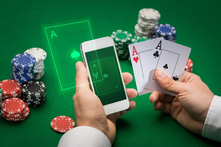 Сида з-а столом в казино, игрок держит в руках два туза и смартфон