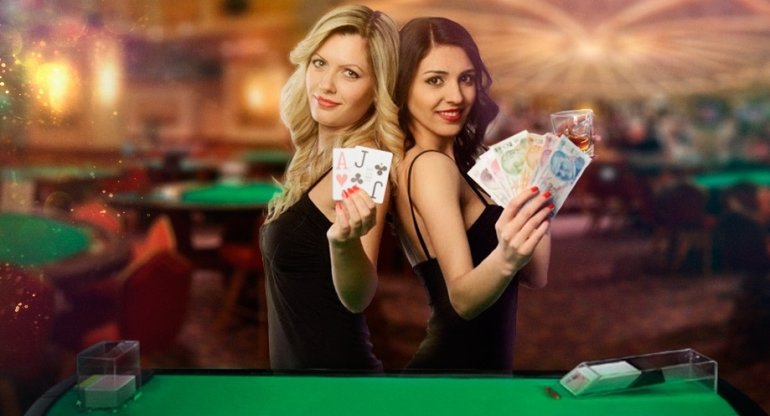 Сексуальные девушки-крупье казино, блондинка и брюнетка, позируют с деньгами в зале казино